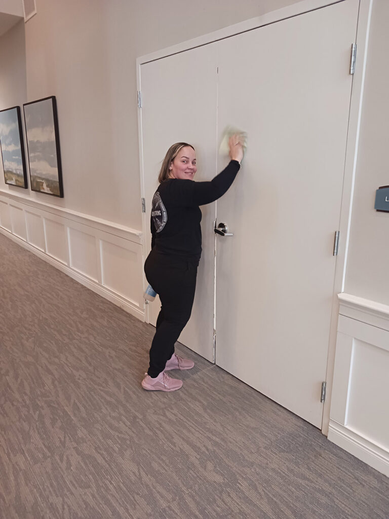 A woman cleaning a white door in a hallway. She's holding a cloth and wiping the door to make it spotless.