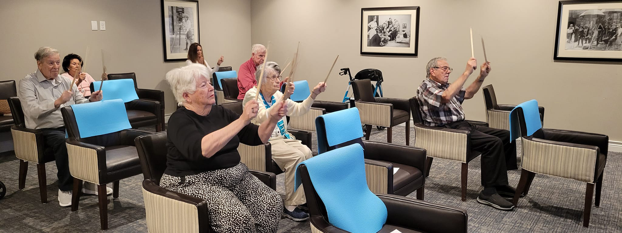 Active seniors participating in a fitness drumming class at Vitalia Westlake Senior Living, arms raised.