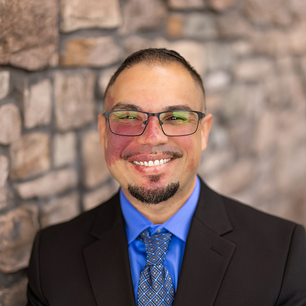 Photo of Eric Pixley, Culinary Director at Vitalia Westlake, smiling in a suit standing against a stone wall backdrop.