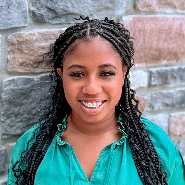 Charletta Richardson, Wellness Director at Vitalia Westlake, smiling in a professional headshot. She has long braided hair, wears a bright green blouse, and stands in front of a multicolored stone wall background.