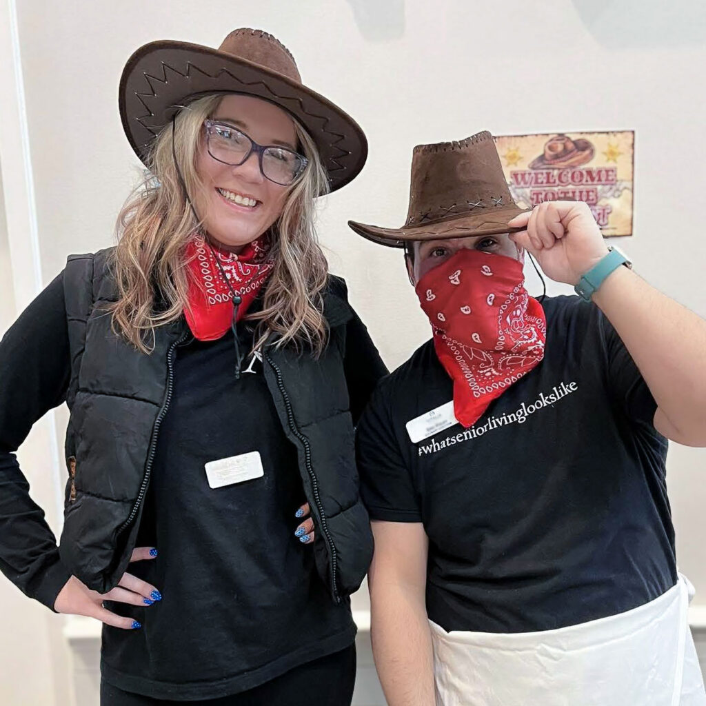 Two team members pose playfully in western wear during a themed event.
