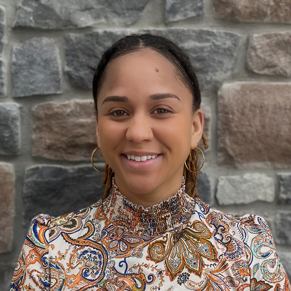 Diontley Harper, Business Office Director at Vitalia Westlake, smiling in a professional headshot, wearing a patterned blouse and hoop earrings, with a stone wall background.