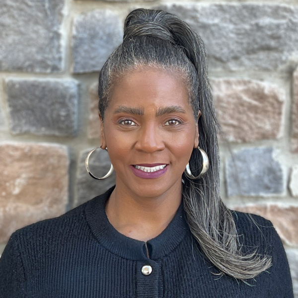 Natashia Moore, Senior Living Director at Vitalia Westlake, smiling in a professional headshot, wearing a black sweater and hoop earrings, standing in front of a stone wall background.