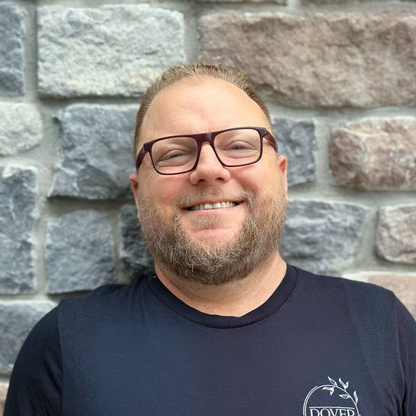 Adam Smith, Culinary Director at Vitalia Westlake, smiling in a professional headshot wearing glasses and a black shirt in front of a gray stone wall.